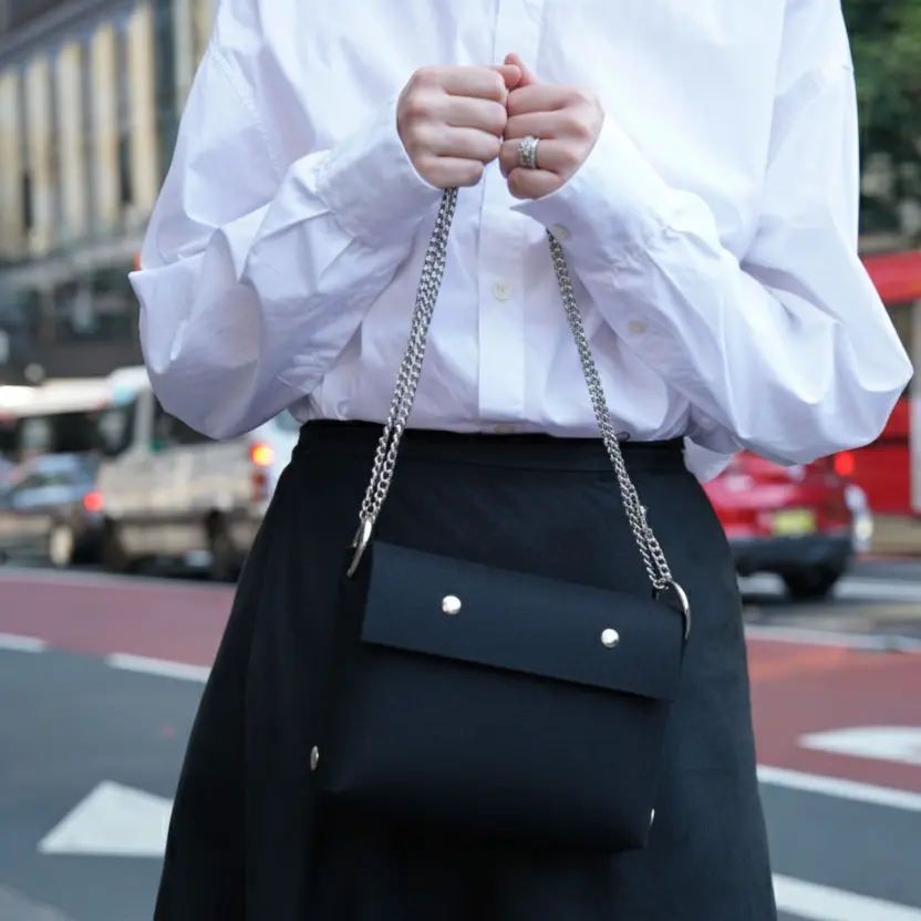 Person wearing a white shirt and black skirt with a black handbag on a street.
