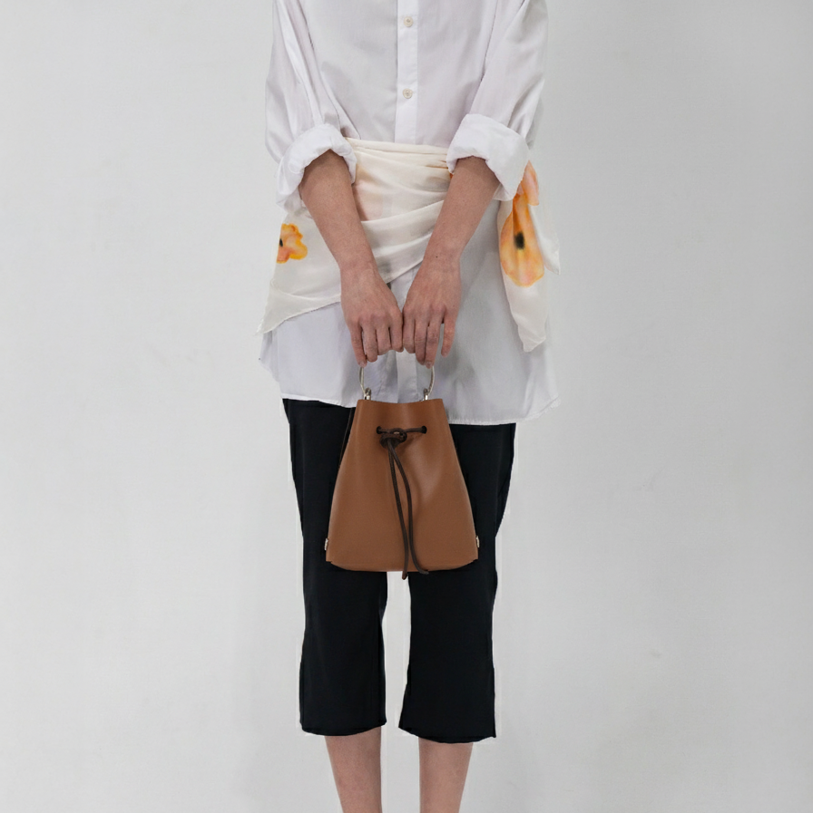 Person wearing a white shirt, black pants, and holding a brown bag on a plain background