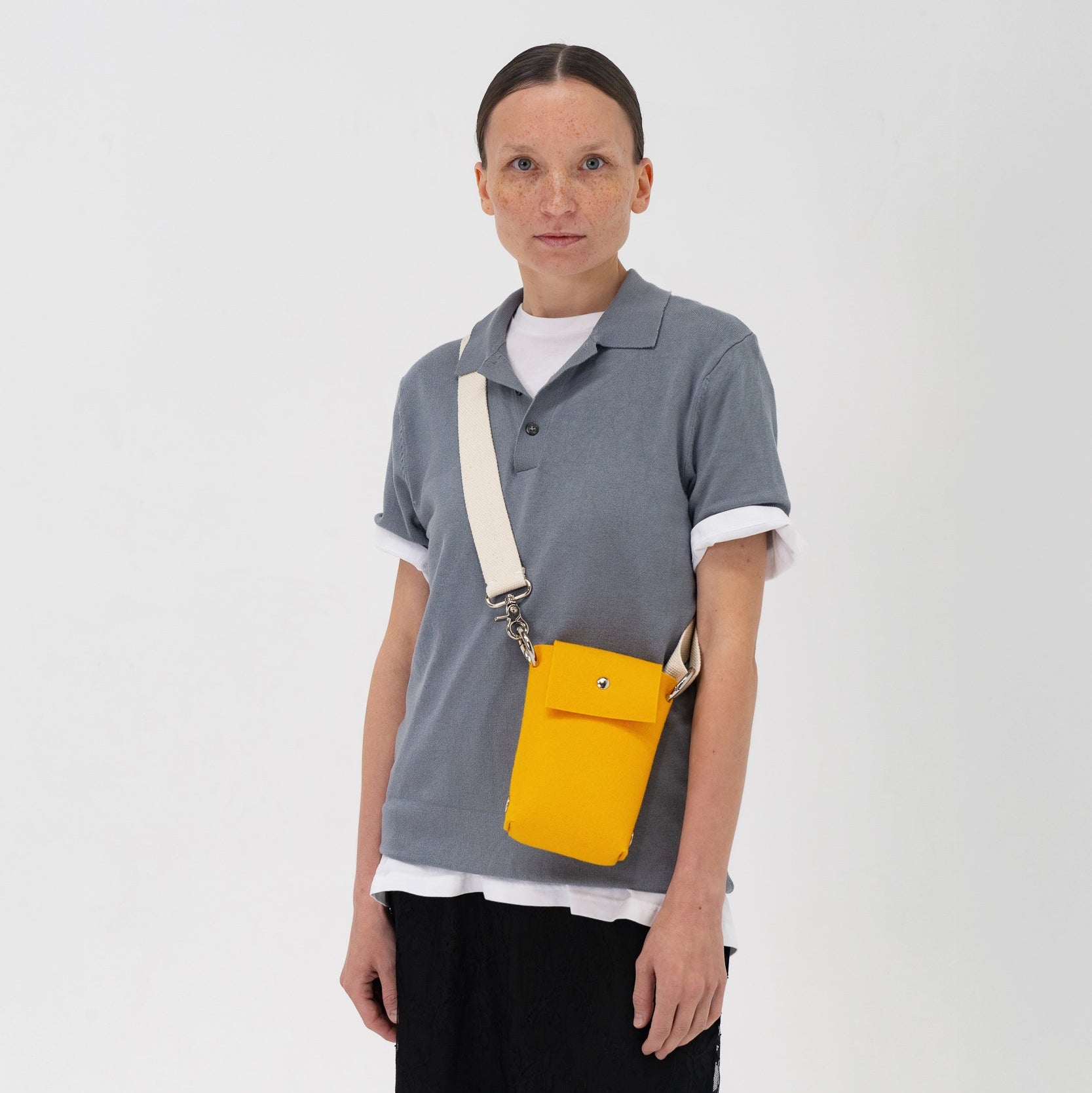 Person wearing a gray polo shirt with a yellow crossbody bag on a white background