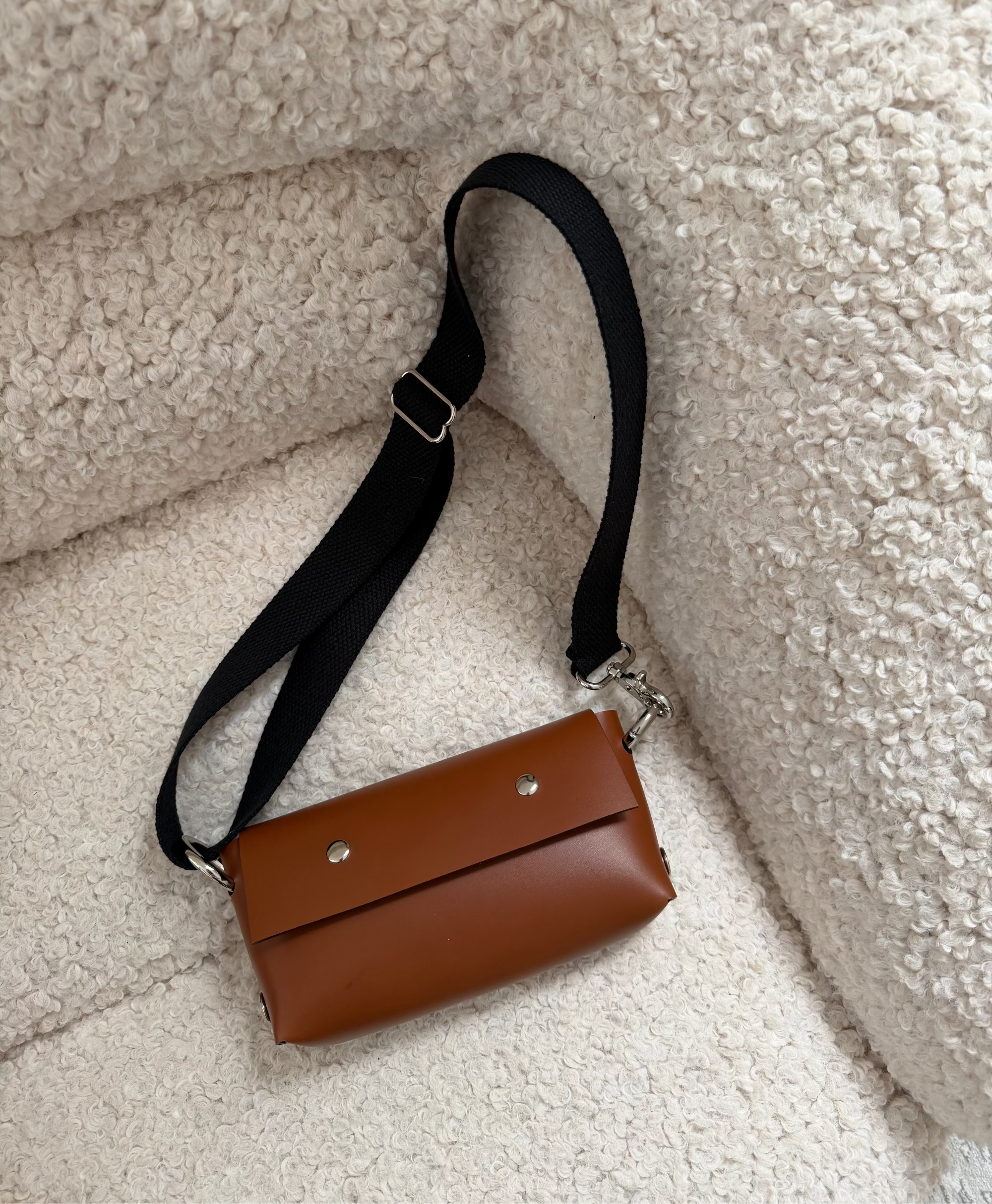 Brown leather bag with a black strap on a textured beige surface