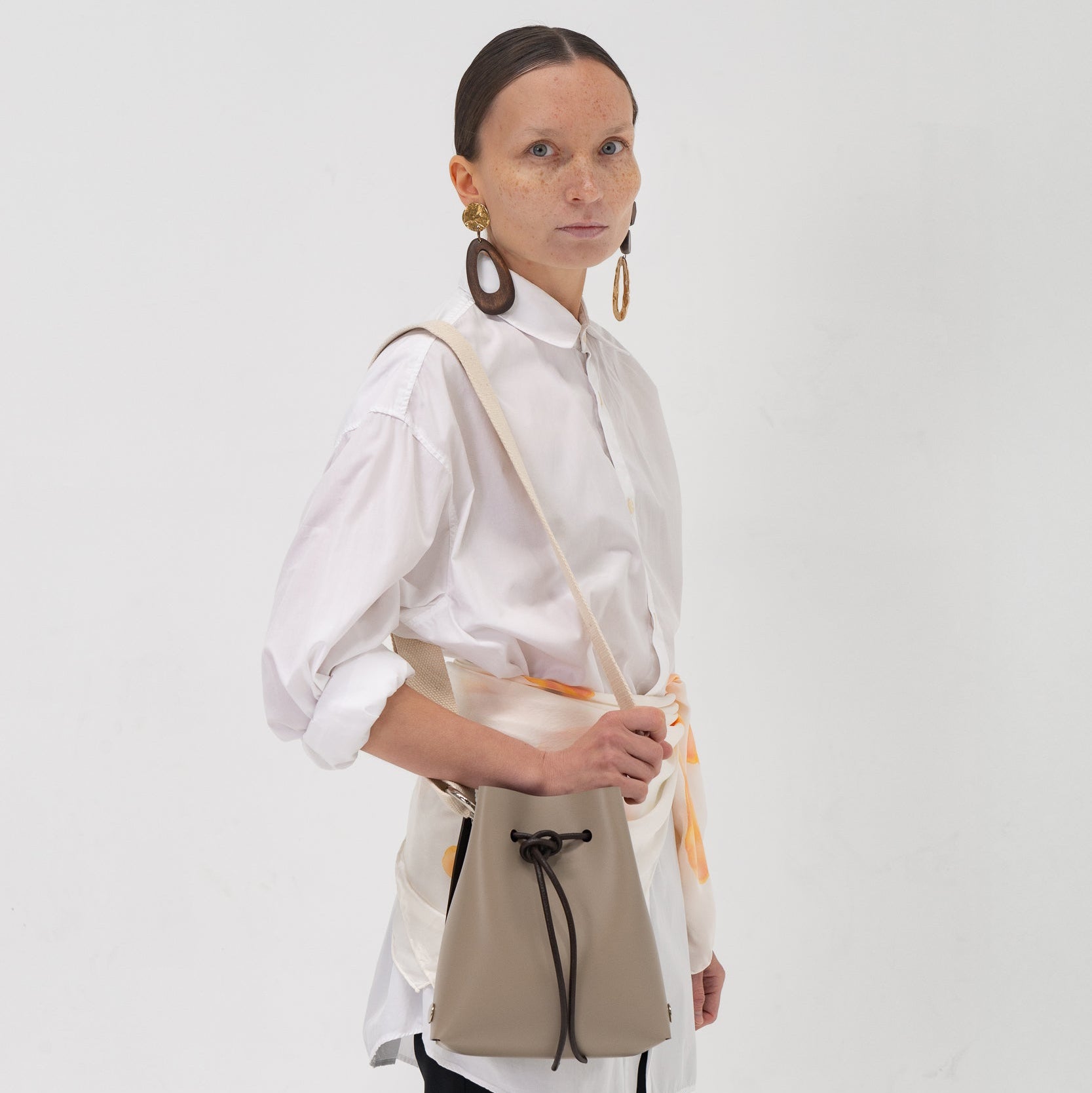 Woman wearing a white shirt and black pants with a beige handbag on a white background