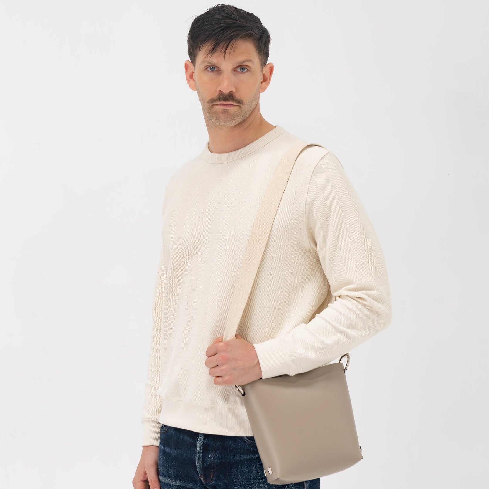 Man holding a beige shoulder bag against a white background