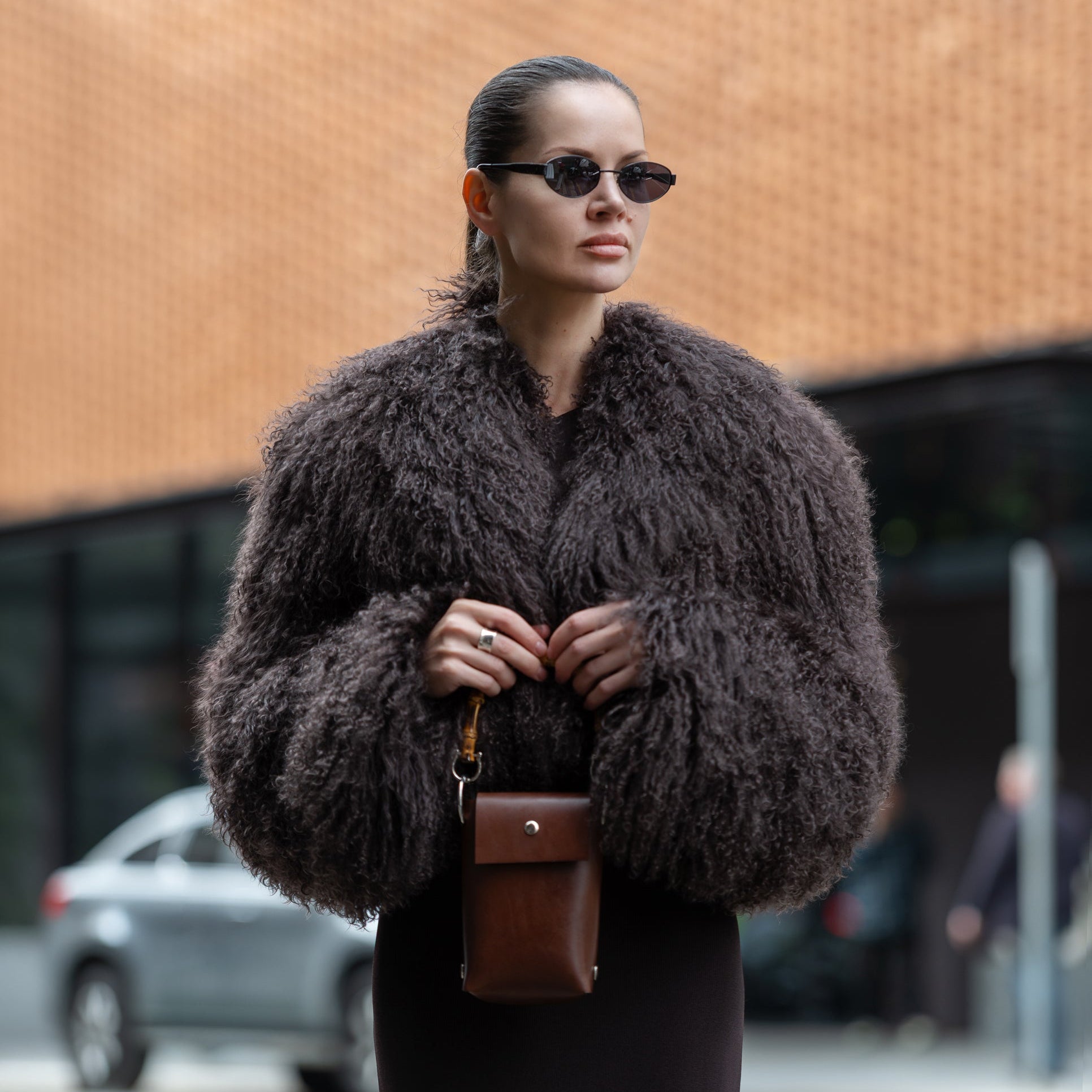 Woman wearing a brown fur coat and sunglasses on a city street.