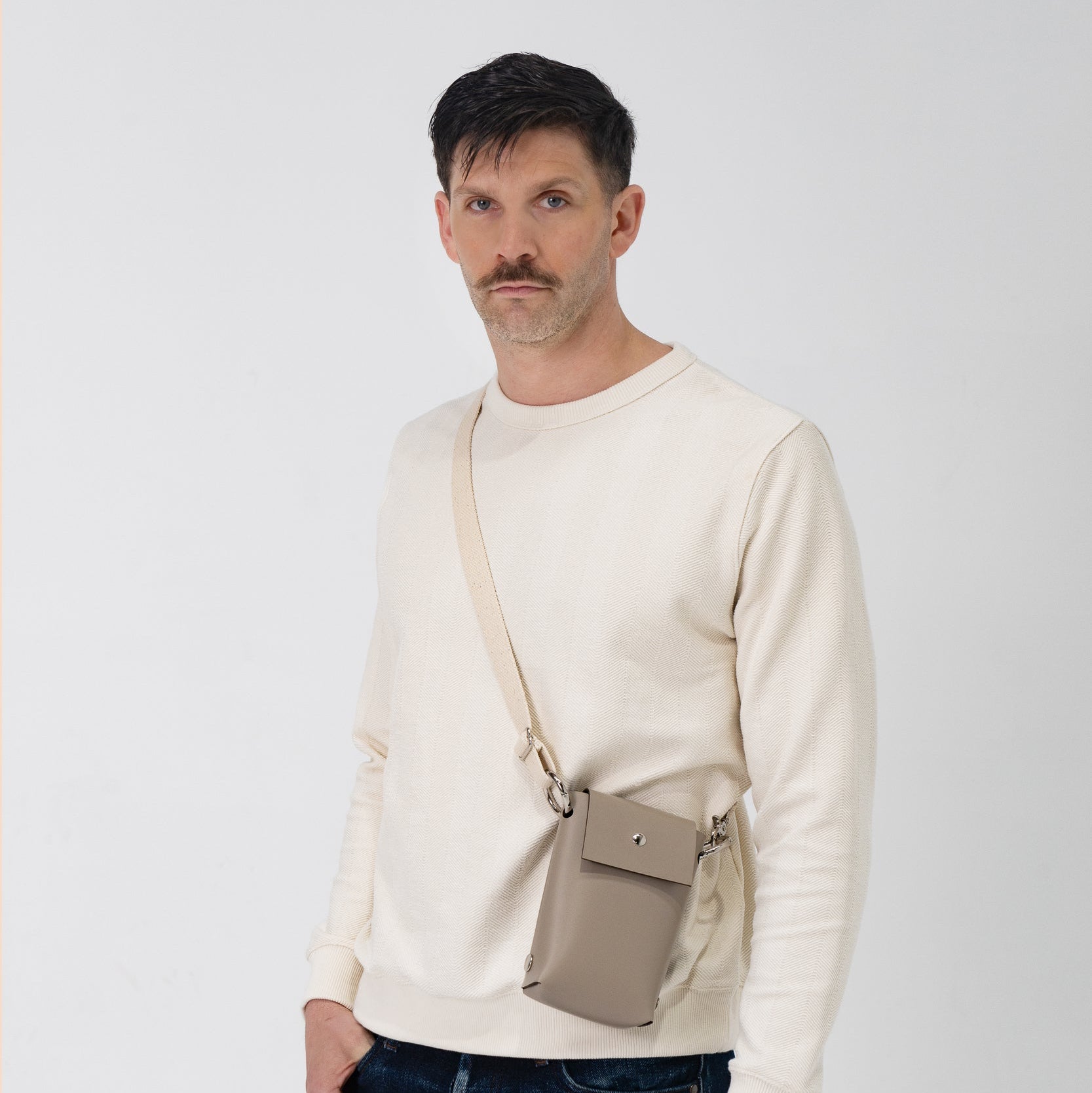 Man wearing a beige sweater with a crossbody bag on a white background