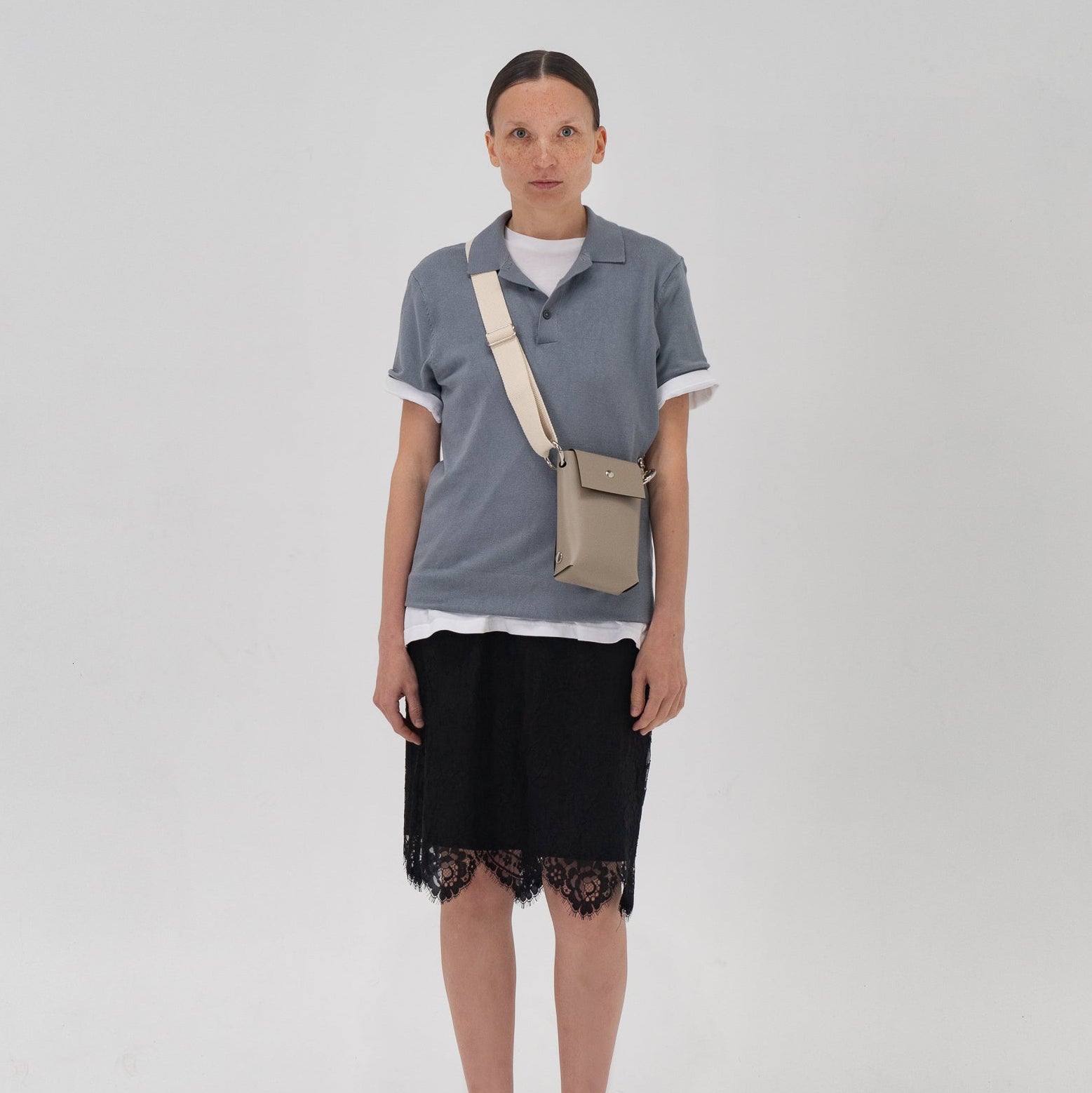 Person wearing a gray shirt, black skirt, and carrying a beige bag on a white background