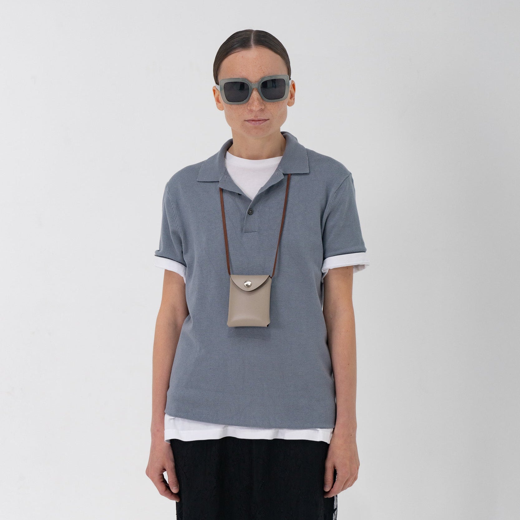 Person wearing a gray polo shirt, white t-shirt, black skirt with lace hem, and sunglasses on a white background.