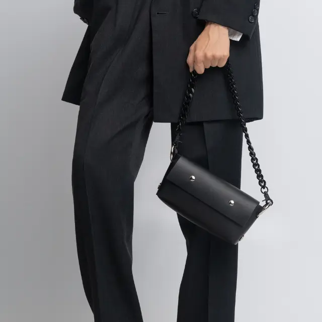 Person wearing a black suit with red high heels holding a black handbag on a light gray background