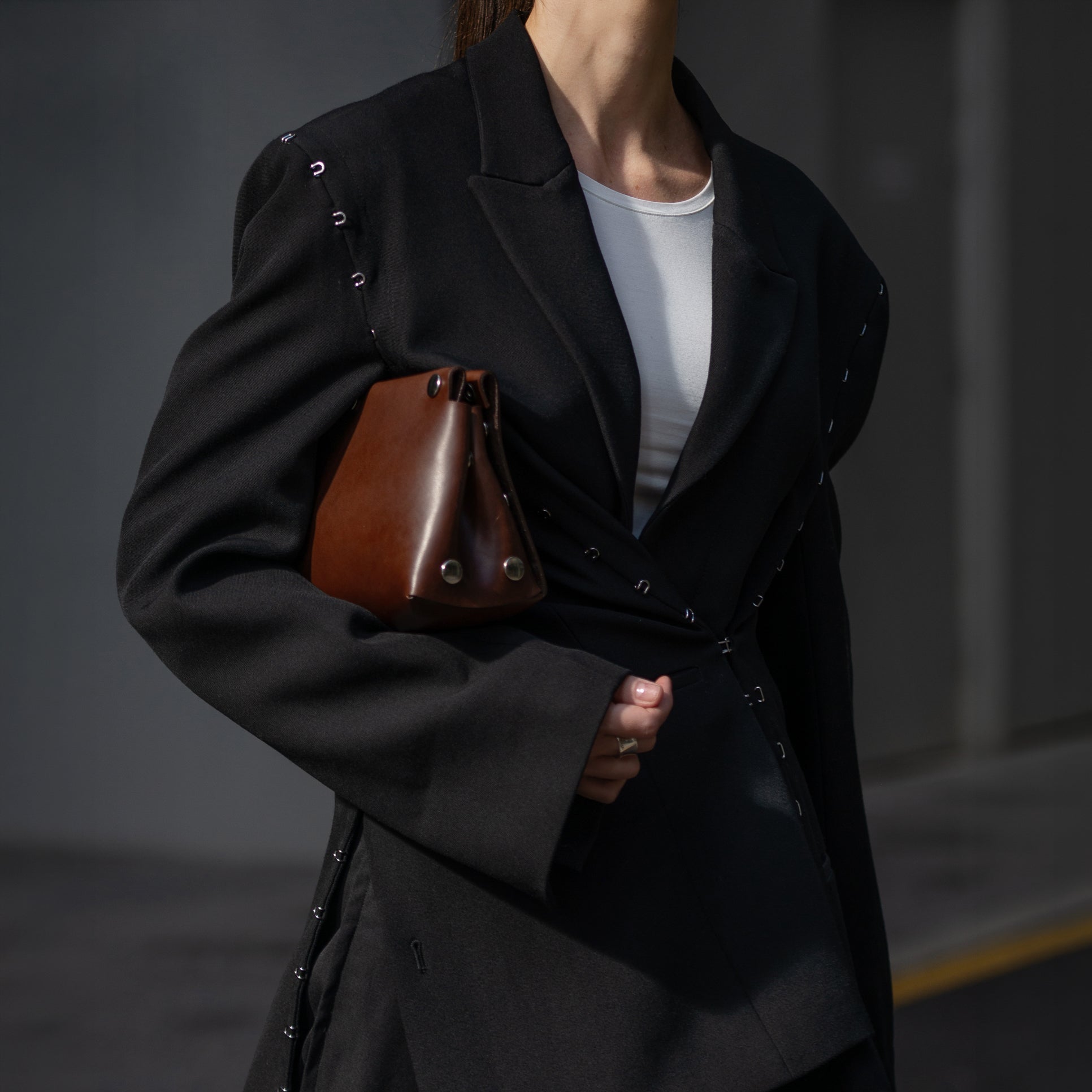 Person wearing a black coat holding a brown leather bag against a dark background
