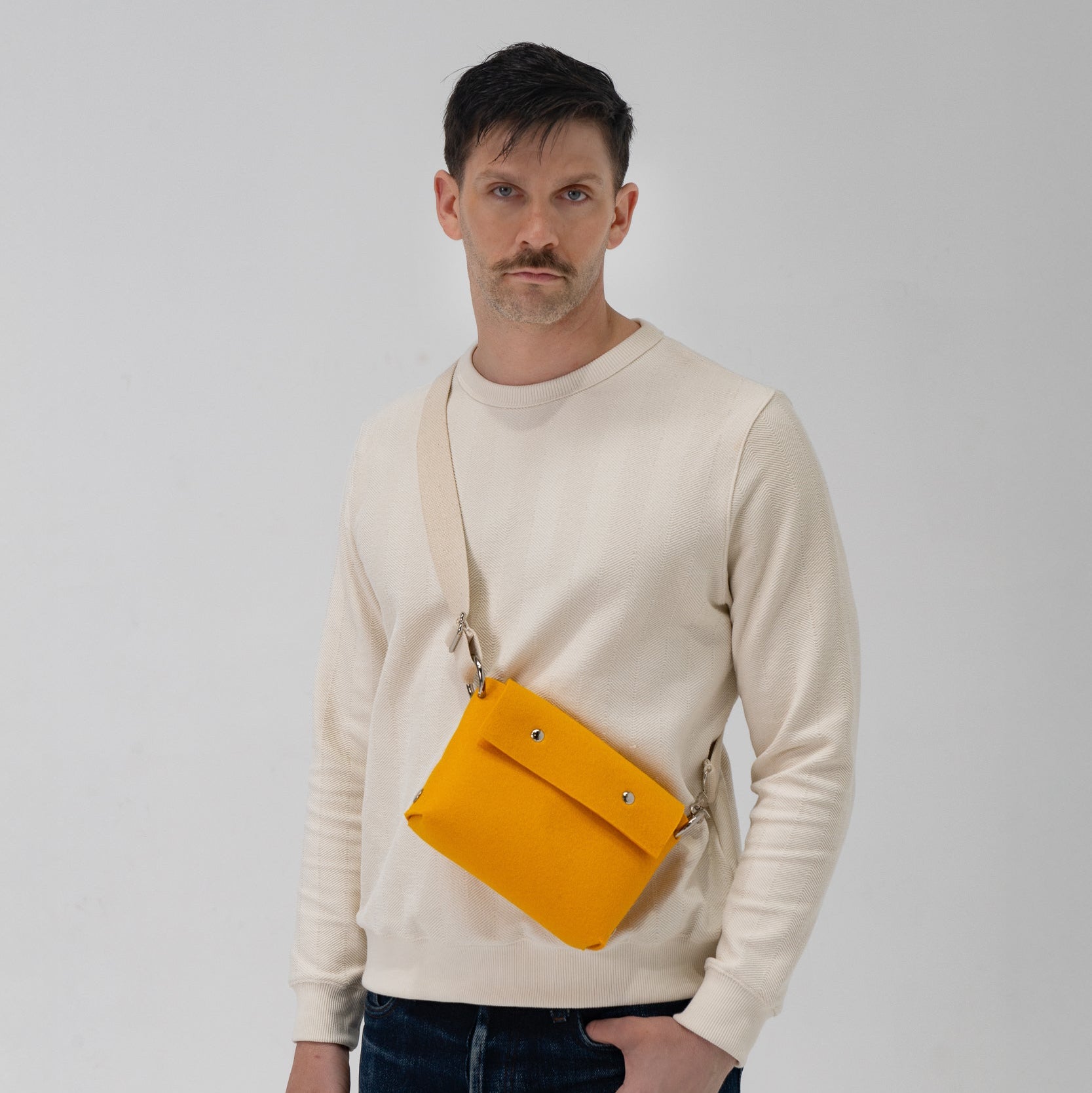 Man wearing a beige sweater with a yellow waist bag on a plain background