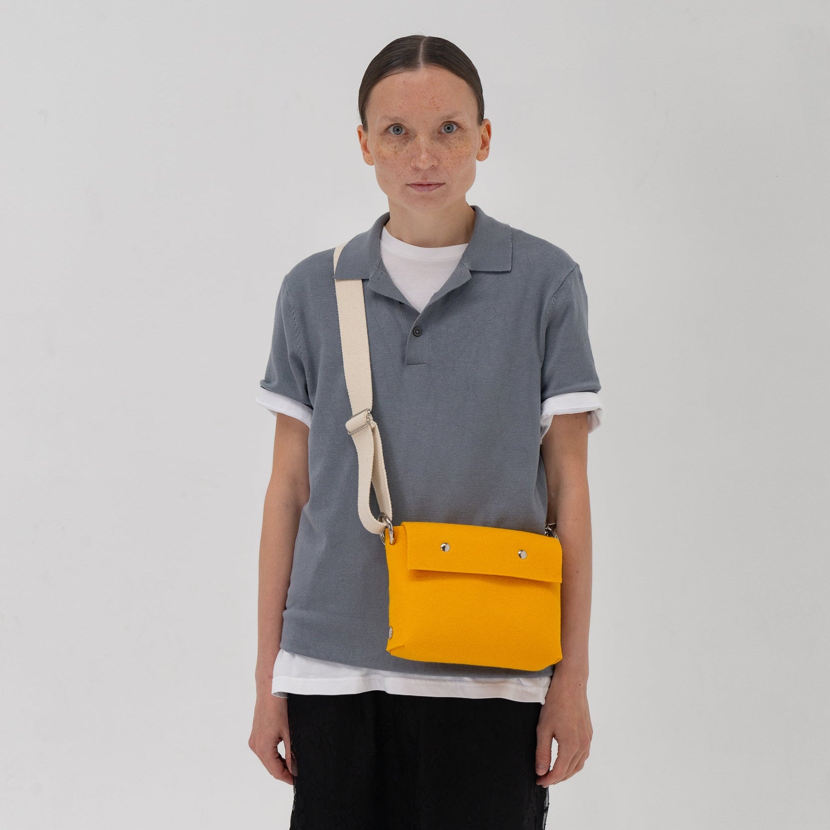 Person wearing a gray polo shirt with a yellow bag over their shoulder on a white background