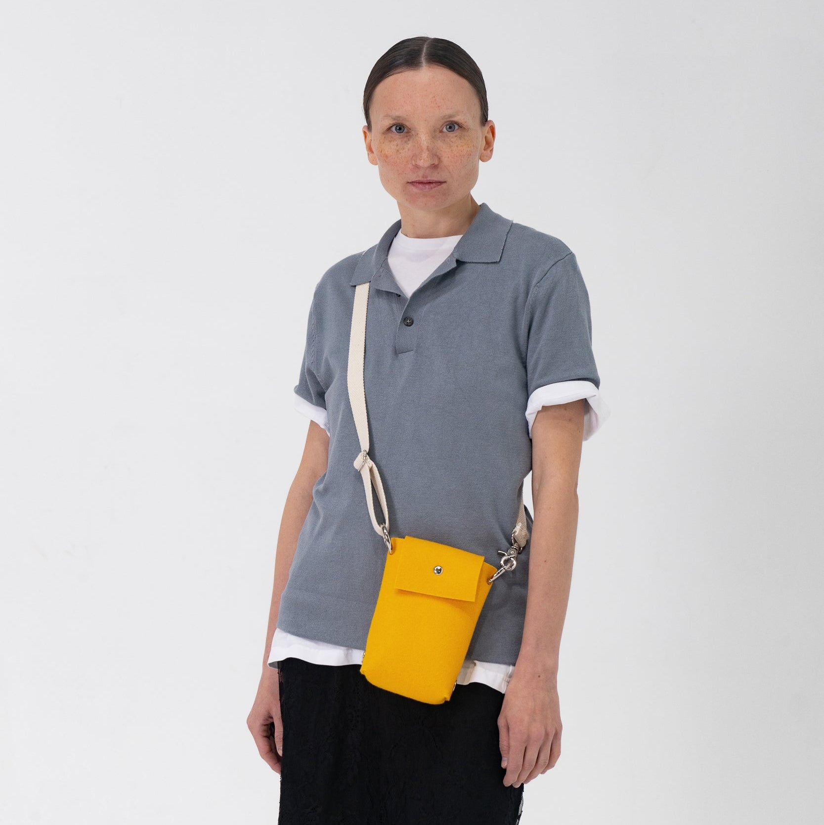 Woman wearing a gray polo shirt and black skirt with a yellow crossbody bag on a white background