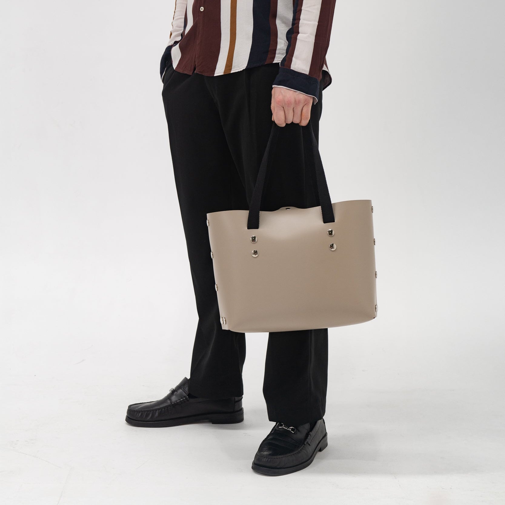Person holding a beige tote bag against a white background
